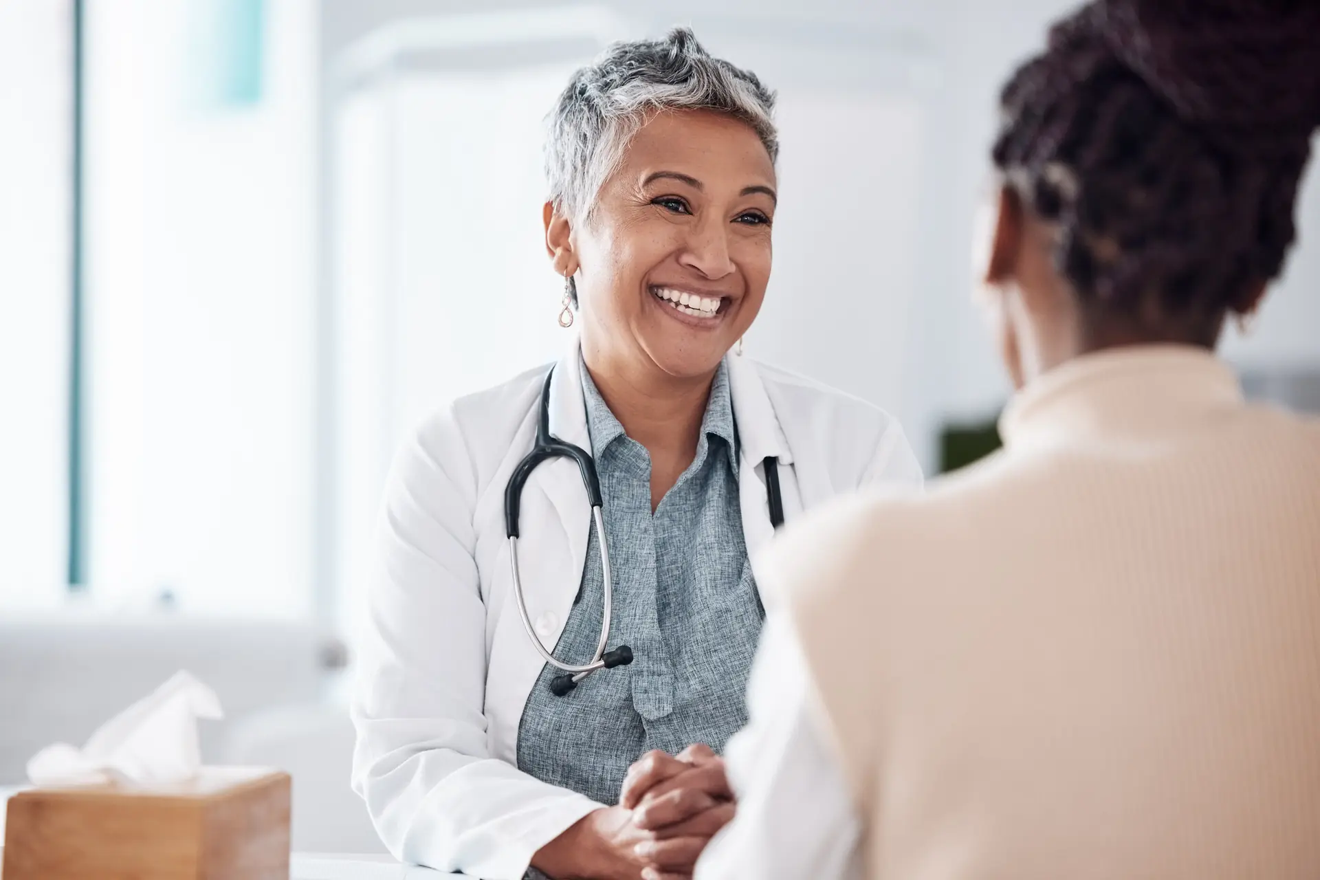 Smiling doctor with stethoscope talking to patient in clinic